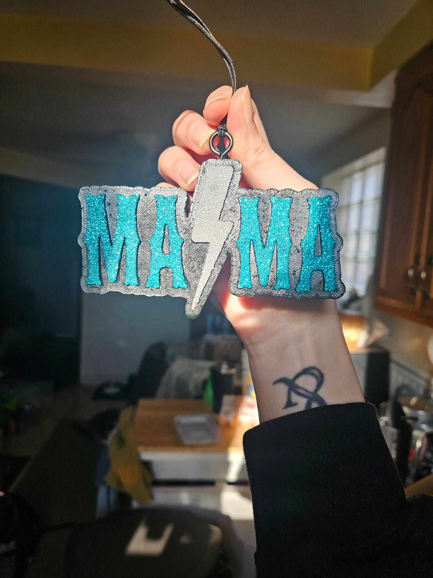 Hand holding a decorative car air freshener with blue and black design, blurred indoor background
